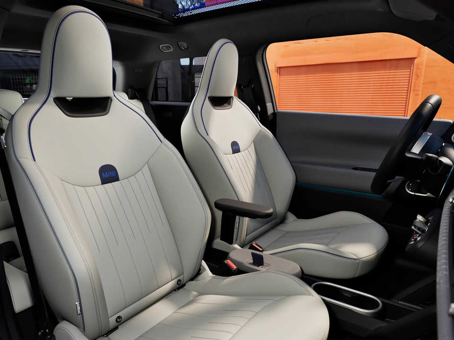 Interior perspective of the all-electric MINI Cooper is showing the dashboard, steering wheel, round display, panorama glassroof  and back of the frontseats