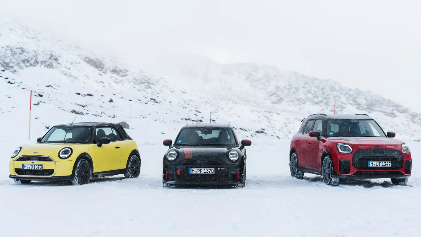 MINI Cooper Convertible in Sunny Side Yellow, MINI John Cooper Works in Midnight Black II, and MINI Countryman Cooper in Chilli Red – stationary on snowy mountain road, front view.