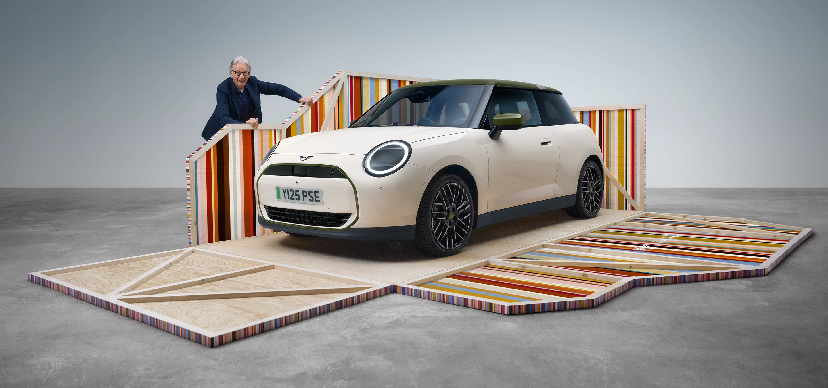 Front side view of the all-electric MINI Cooper Paul Smith Edition in Inspired White with designer Paul Smith.